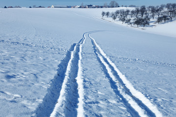 Snowy field on a sunny day with traces of a car on it