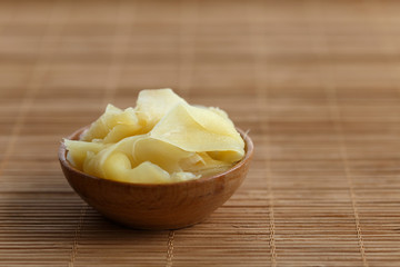 Pickled ginger slices in wooden bowl on bamboo mat.