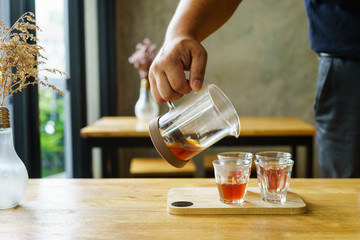 man pouring fresh brewed coffee into glass on wood table
