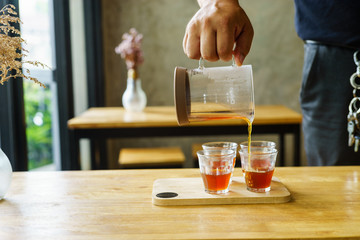 man pouring fresh brewed coffee into glass on wood table