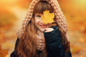 autumn outdoor portrait of beautiful happy child girl walking in park or forest in warm knitted scarf