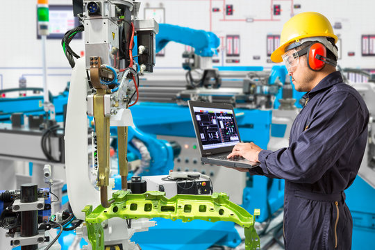 Engineer using laptop computer maintenance automatic robotic hand machine tool in automotive industry manufacturing factory