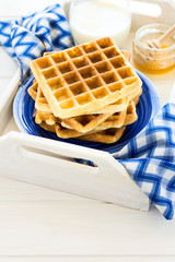 Healthy breakfast: Belgian waffles with blackberries, honey and milk decorated mint leaves and blue napkin on white wooden salver. Warm light. Selective focus