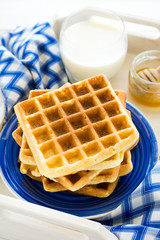 Healthy breakfast: Belgian waffles with blackberries, honey and milk decorated mint leaves and blue napkin on white wooden salver. Warm light. Selective focus