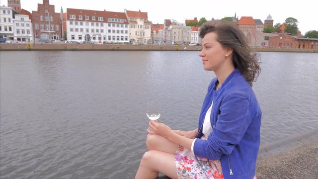 Pretty young woman spending time on embankment, drinking wine and enjoying good weather