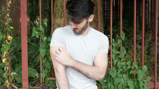 Handsome young man outdoor getting bitten by mosquito, and scratching his arm