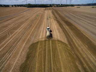 Naklejka premium aerial view of a tractor with a trailer fertilizes a freshly plowed agriculural field with manure in germany