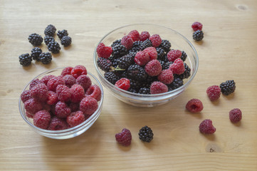 Raspberries and blackberries in a glass jar on a wooden table.