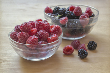 Raspberries and blackberries in a glass jar on a wooden table.