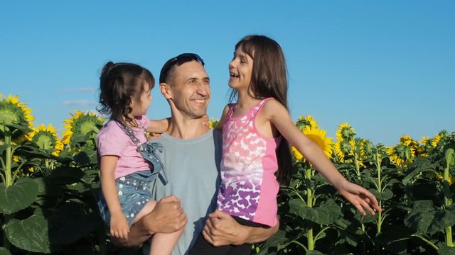 Happy family on the field with sunflowers. The father hugs his daughters.