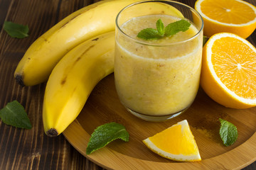 Smoothie from banana and orange on the cutting board on the brown wooden background  