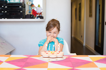 Obraz na płótnie Canvas happy three years old blonde child smiling watching burning candles on birthday cake on colorful tablecloth at home 