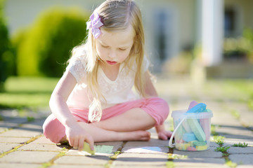Cute little girl drawing with colorful chalks on a sidewalk. Summer activity for small kids. © MNStudio