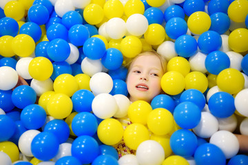 Fototapeta na wymiar Happy little girl having fun in ball pit in kids indoor play center. Child playing with colorful balls in playground ball pool.