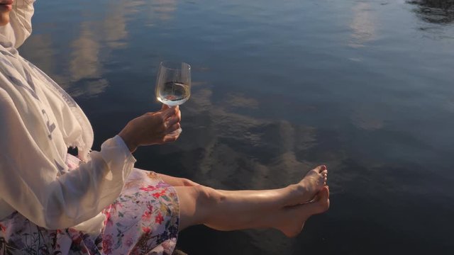 Pretty young woman outdoors drinking wine on embankment of the river