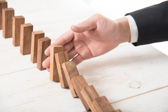 Businessman hand trying to stop toppling dominoes on wood,stop domino effect