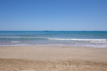 Fototapeta na wymiar landscape of Mediterranean Sea from sand shore beach of Grao of Castellon, in Valencia, Spain, Europe. Blue clear sky, and great cargo boats sailing in the horizon 