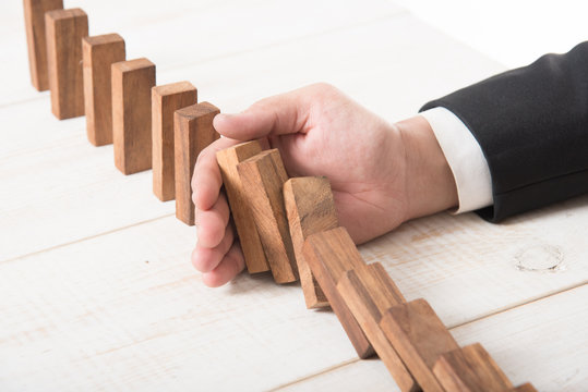 Businessman hand trying to stop toppling dominoes on wood,stop domino effect