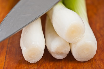 Macro of the cut endes of four green onions with the blade of a chefs knife on a wood cutting board