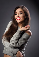 Joying beautiful brunette woman with long hair style in grey fashion sweater looking with toothy smiling on dark shadow background