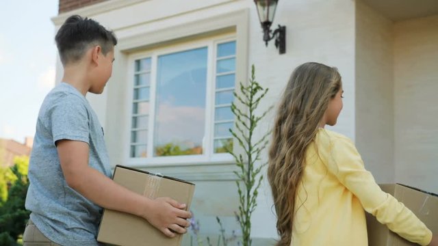Portrait of happy young caucasian family moving to the new modern light home with big cardboard box, walking throught the garden during the sunset. Close up.