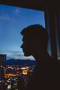 Silhouette of man at dark office window, looking out over cityscape lights