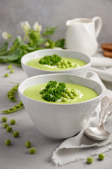 Green pea soup in bowls on grey concrete or stone background, selective focus