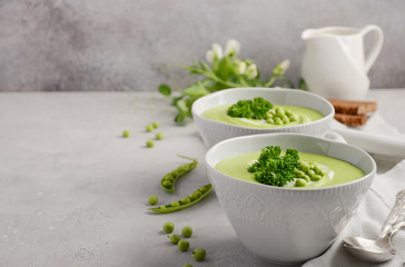 Green pea soup in bowls on grey concrete or stone background, selective focus, copy space