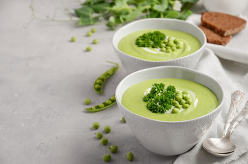 Green pea soup in bowls on grey concrete or stone background, selective focus, copy space