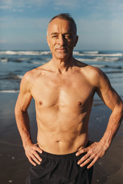 Active senior man - in great shape - standing shirtless on beach in morning sunshine
