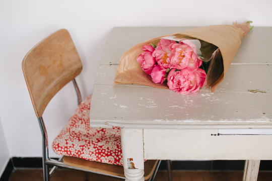 Table with bright pink peonies wrapped in brown paper