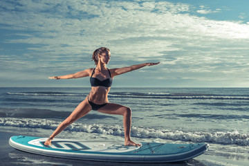 Beautiful sporty woman practicing SUP yoga at sunrise.