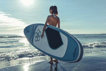 Beautiful sporty girl with the sup surfboard at sea beach.