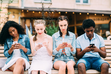 Series photo of group multiethnic hipster teenagers friends looking in smart phones while sitting on the bench outdoor in ciity center.People, leisure, friendship, technology and communication concept
