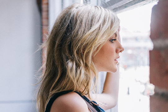 Young blonde female with hand on window looking out in thought