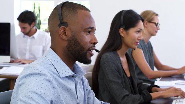 Black man in headset smiles to camera in open plan office