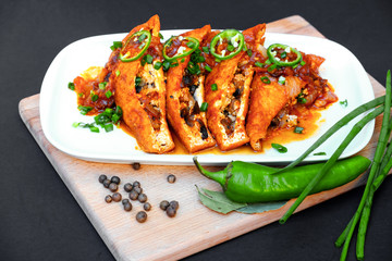 Asian food fried tofu with mushrooms and tomato close-up on a plate on a table. Green hot chili peppers and green onions.