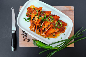 Asian food fried tofu with mushrooms and tomato close-up on a plate on a table. Green hot chili peppers and green onions.