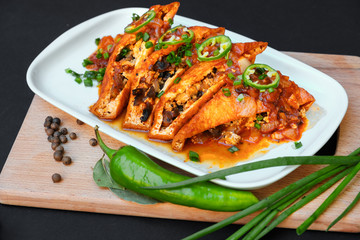 Asian food fried tofu with mushrooms and tomato close-up on a plate on a table. Green hot chili peppers and green onions.