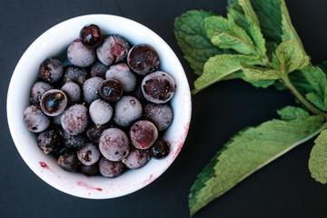 Frozen berries on a black background. With a sprig of mint