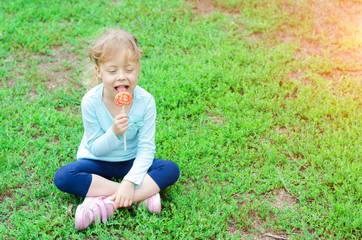 Fototapeta premium Happy little girl with a lollipop, free space. A beautiful child with a lollipop.