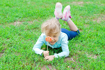 Happy little girl with a lollipop lies on a green glade, free space for your text.