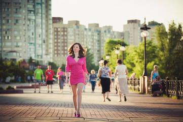 Fototapeta na wymiar Girl in a pink dress is walking around the city
