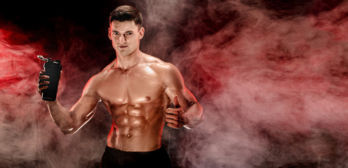 Muscular man with protein drink in shaker over dark smoke background