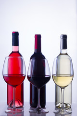 Set of three wine glasses and bottles with red, white and rose wine