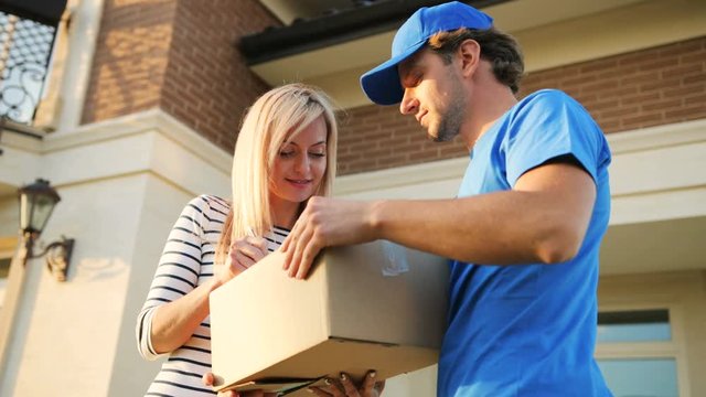 Attractive young woman signing the documents for getting package from the courier. View from the bottom.