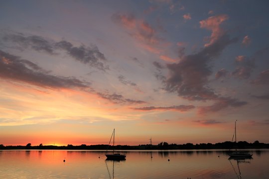 magisches Lich mit angestrahlten Wolken am malerischen Abendhimmel, Segelboot auf der Schlei