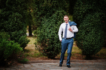 Portrait of a handsome groom posing in the park with trees on the background on his wedding day.