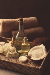 Spa oil in bottles, candle, coconuts and flowers on tray