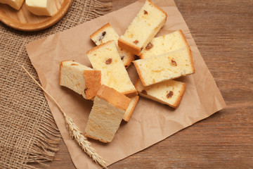 Paper with delicious butter cake and wheat ear on wooden table